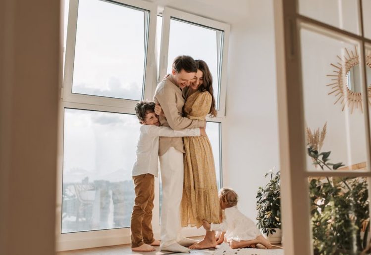 A happy family embracing near a large window in a bright, cozy room filled with natural light.