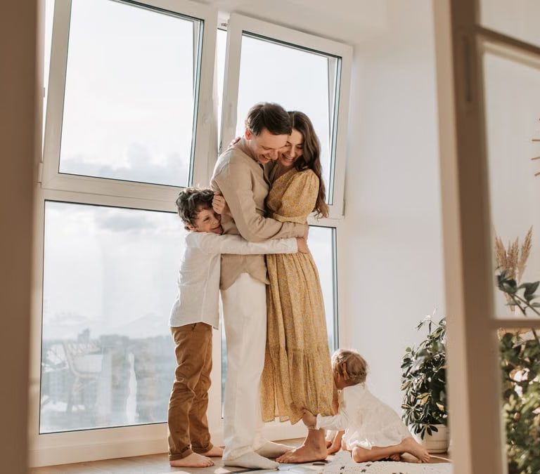 A happy family embracing near a large window in a bright, cozy room filled with natural light.