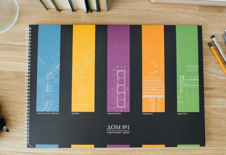 Design and architecture workbook with colorful blueprints on a wooden desk.