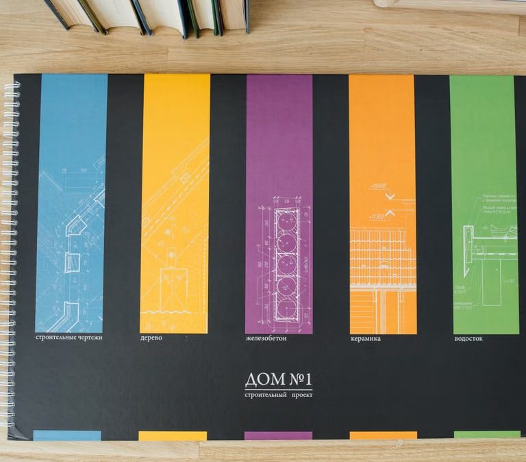 Design and architecture workbook with colorful blueprints on a wooden desk.